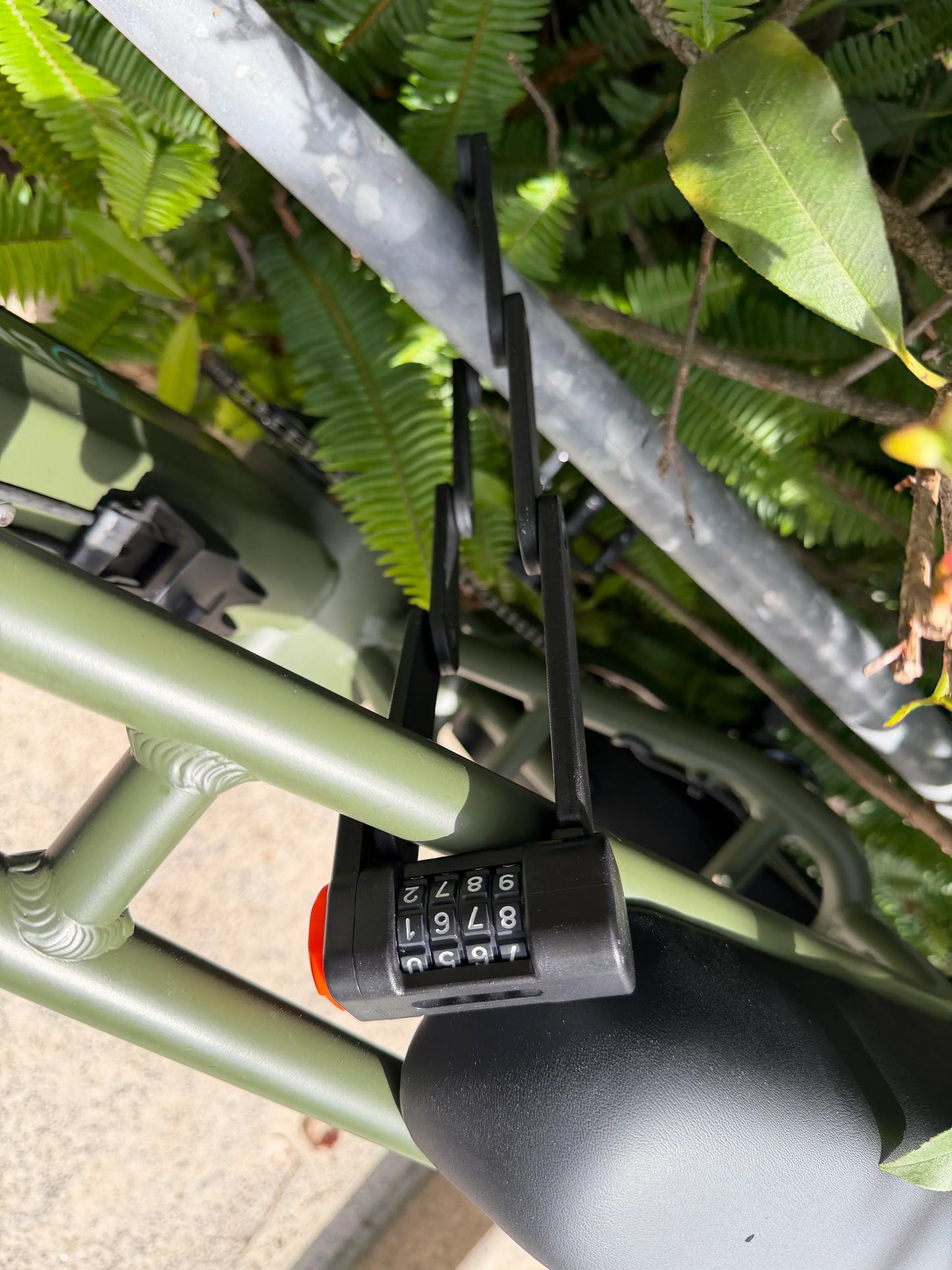 Green e-bike frame with combination lock, surrounded by lush greenery