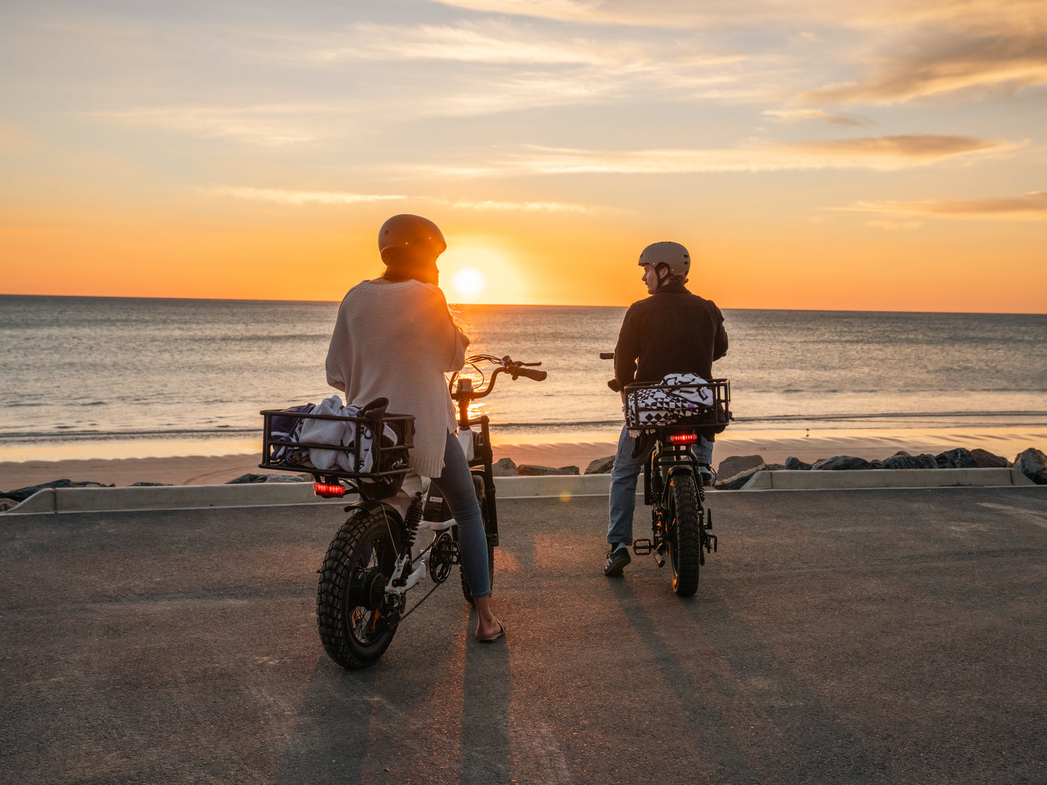 Couple riding The Captain electric cruisers into the sunset along the coast