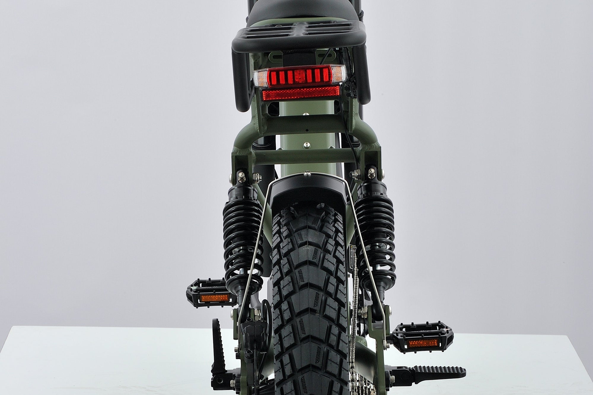 Rear view of an electric  bike with a black frame, high handlebars, a black seat, and a rugged knobby tire, photographed on a white studio background.