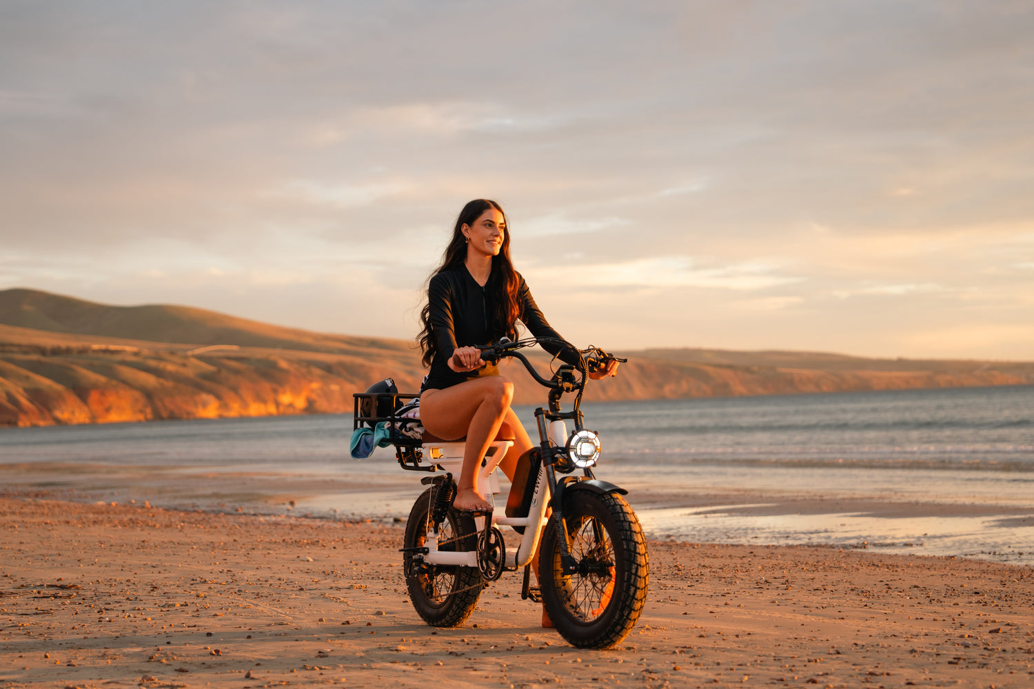 Woman riding The Captain white street-legal electric cruiser on the beach at golden hour